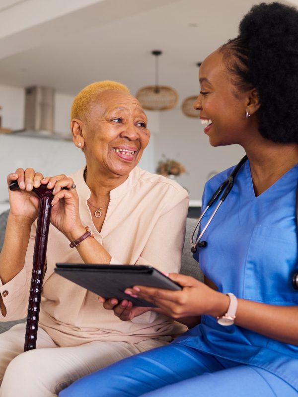 Health consultation, nurse and black woman with tablet for medical information or advice online. Smile, conversation and an African nurse helping a senior patient with healthcare on an app in a house.